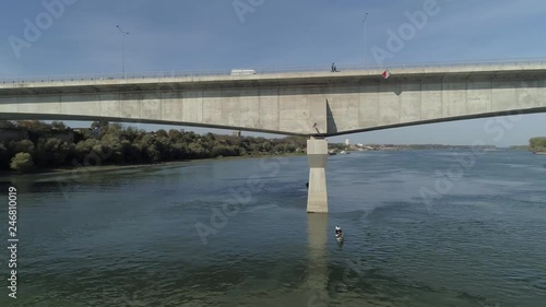 Aerial HD shot showing a large concrete bridge over Danube in Belgrade, Zemun and some fishermen in a small boat beneath on a nice sunny day. photo