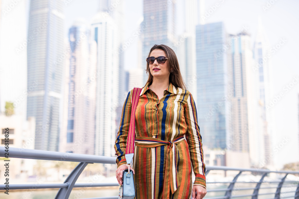 Young woman in sunglasses standing in Marina Walk Dubai and looking at the city
