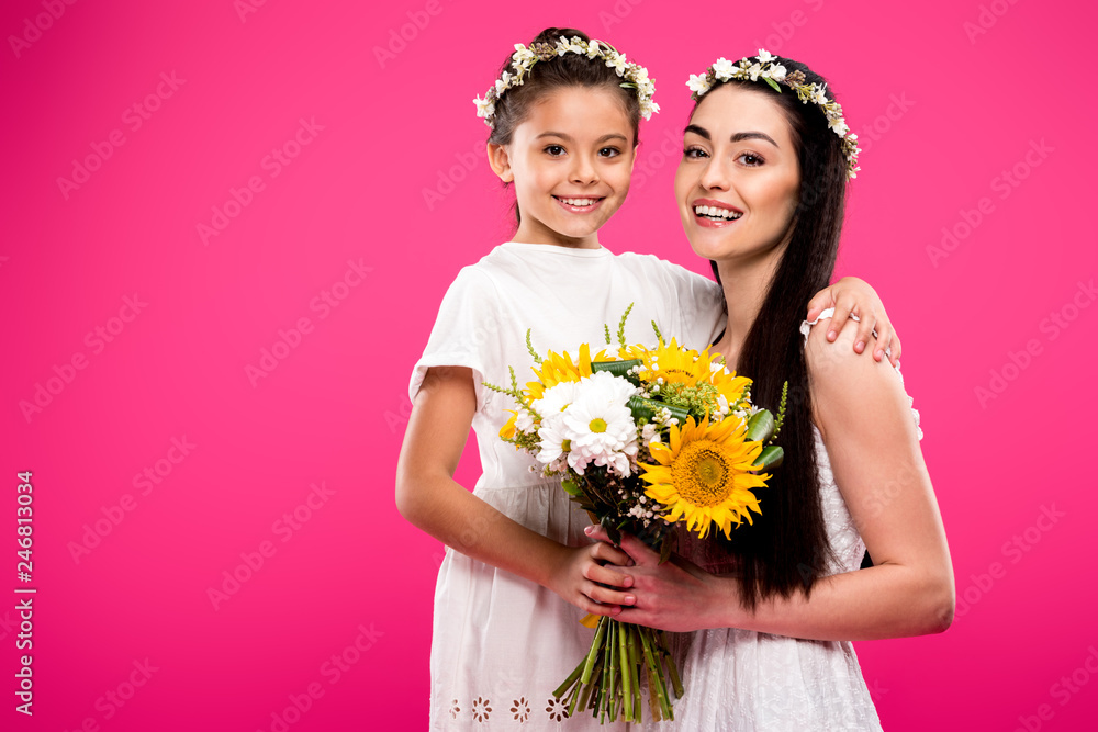 beautiful happy mother and daughter in white dresses and floral wreaths holding flower bouquet and smiling at camera isolated on pink beautiful happy mother and daughter in white dresses and floral wreaths holding flower bouquet and smiling at camera isolated on pink
