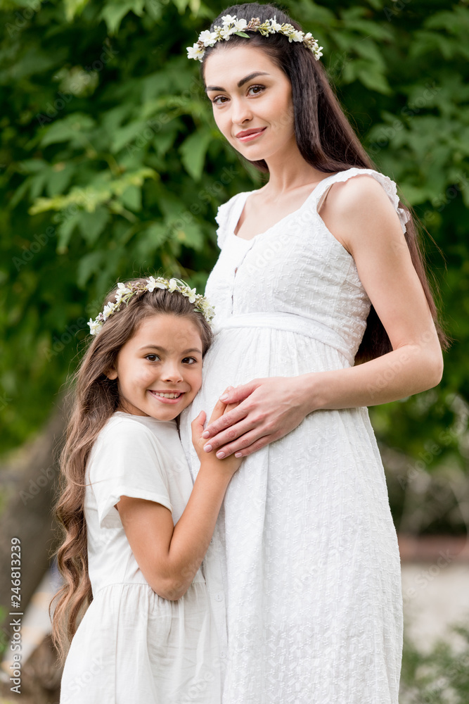 adorable happy child hugging pregnant mother and smiling at camera in park adorable happy child hugging pregnant mother and smiling at camera in park