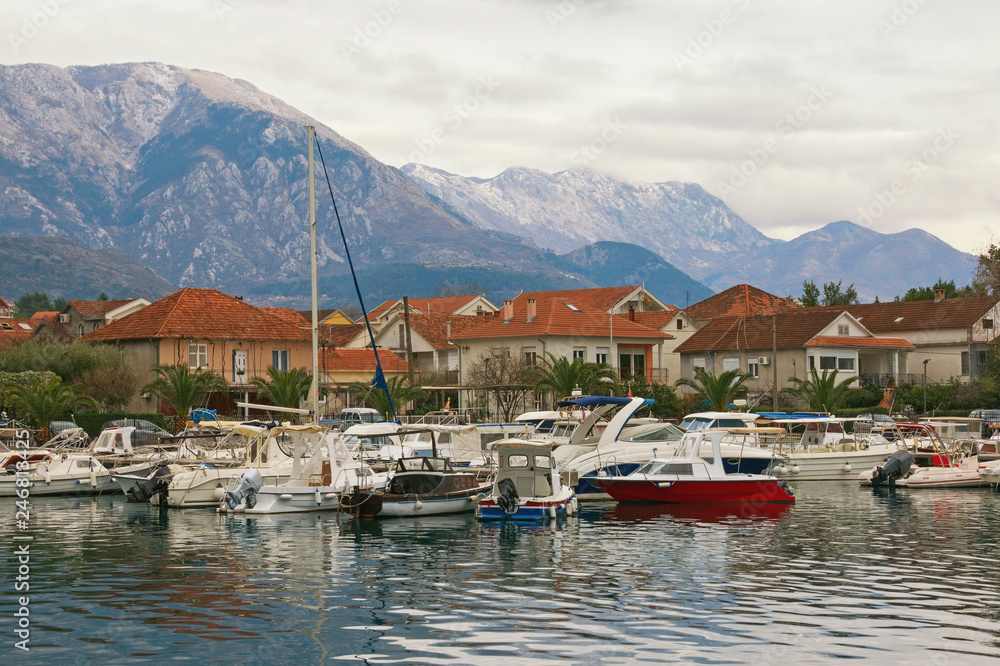 Cloudy winter day. Small marina for fishing boats at foot of mountains.   Montenegro, Bay of Kotor. Marina Kalimanj in Tivat city and peaks of Lovcen mountains
