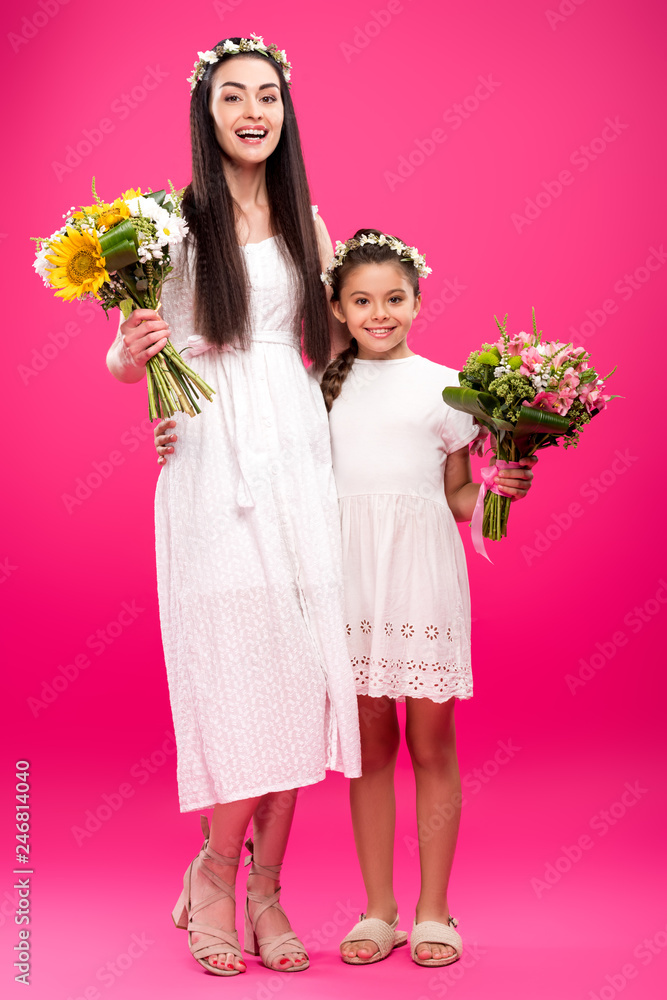 happy mother and daughter in white dresses and floral wreaths holding beautiful bouquets on pink happy mother and daughter in white dresses and floral wreaths holding beautiful bouquets on pink