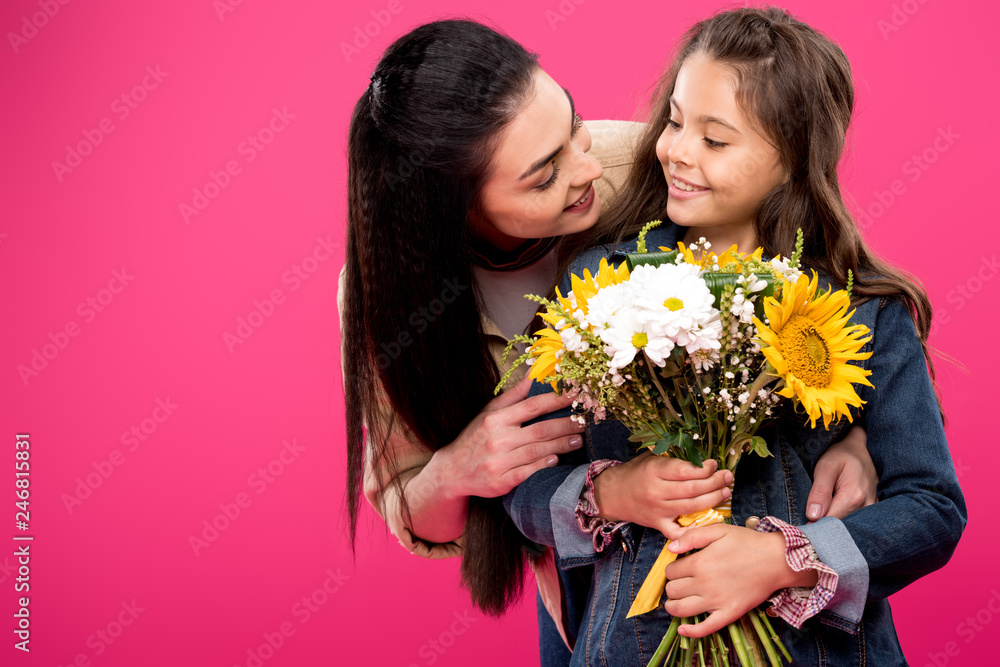 happy mother looking at cute smiling daughter holding flower bouquet isolated on pink happy mother looking at cute smiling daughter holding flower bouquet isolated on pink