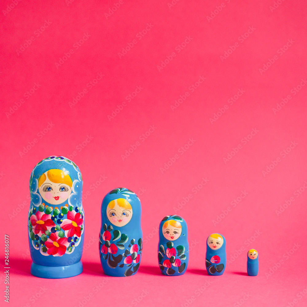 A line of five stacking Russian dolls against a bright pink background