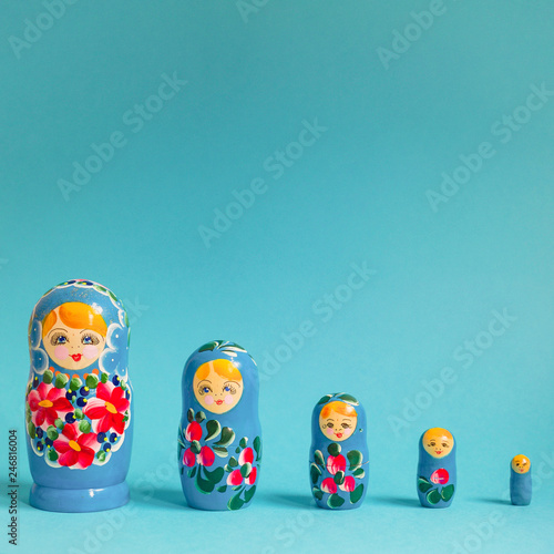 A row of five stacking Russian dolls, painted with a blue and pink pattern, against a bright blue background