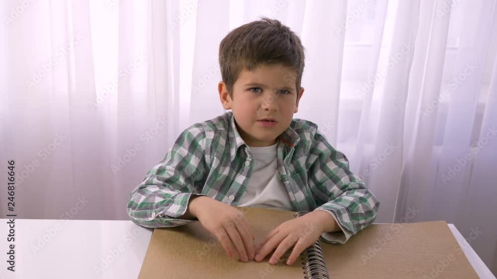Visually impaired small boy reading braille book with symbols font for blind sitting at table indoors Visually impaired small boy reading braille book with symbols font for blind sitting at table indoors