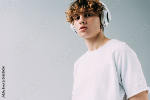 handsome man with curly hair listening music in headphones isolated on grey