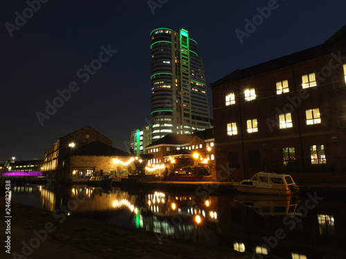leeds canal wharf at night with brightly illuminated buildings and lock reflected in the water and glowing against a dark sky