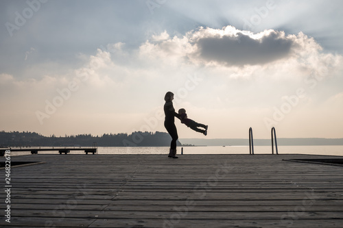 Mother spinning her toddler son on a wooden pier over the sea