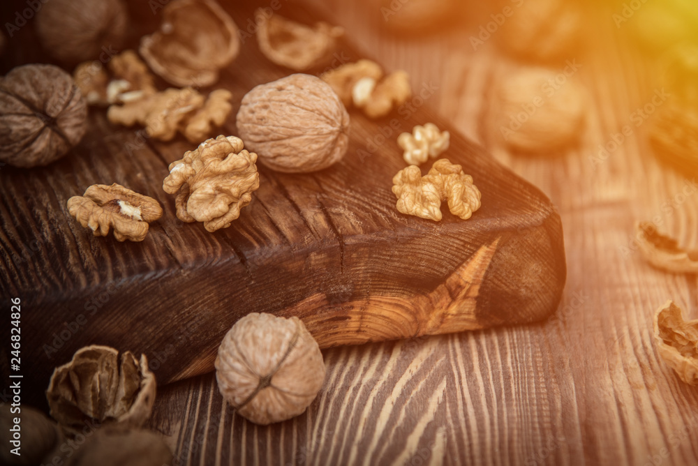 Obraz premium Close up view composition of walnut kernels and whole walnuts on rustic cuting desk. Selective focus. toned