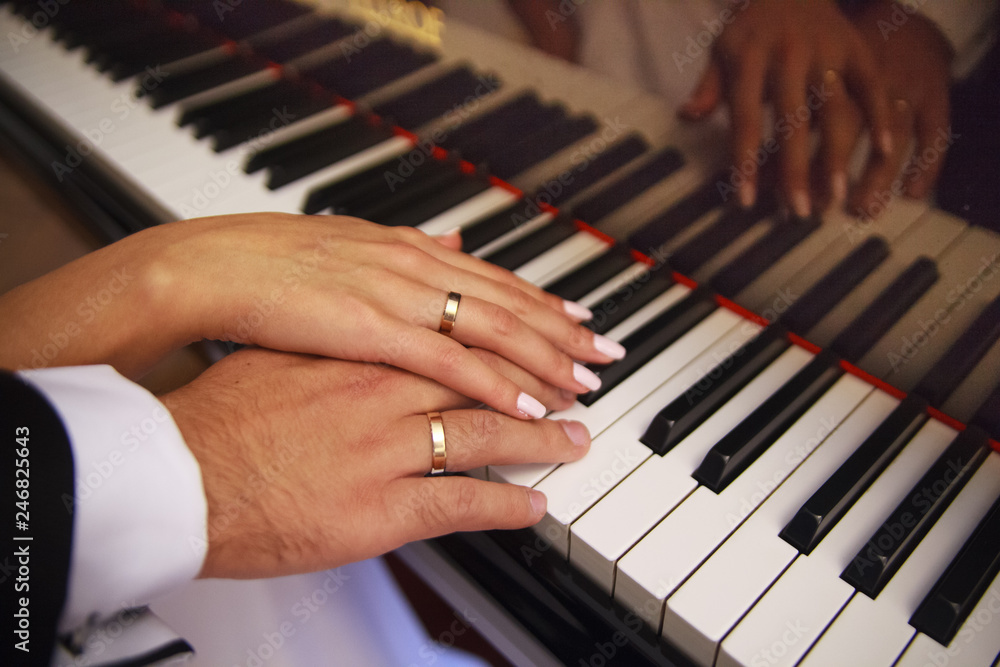 Fototapeta premium Two hands on the piano. Play. The piano keys. Wedding. A touch of hands. Wedding rings. Closeup