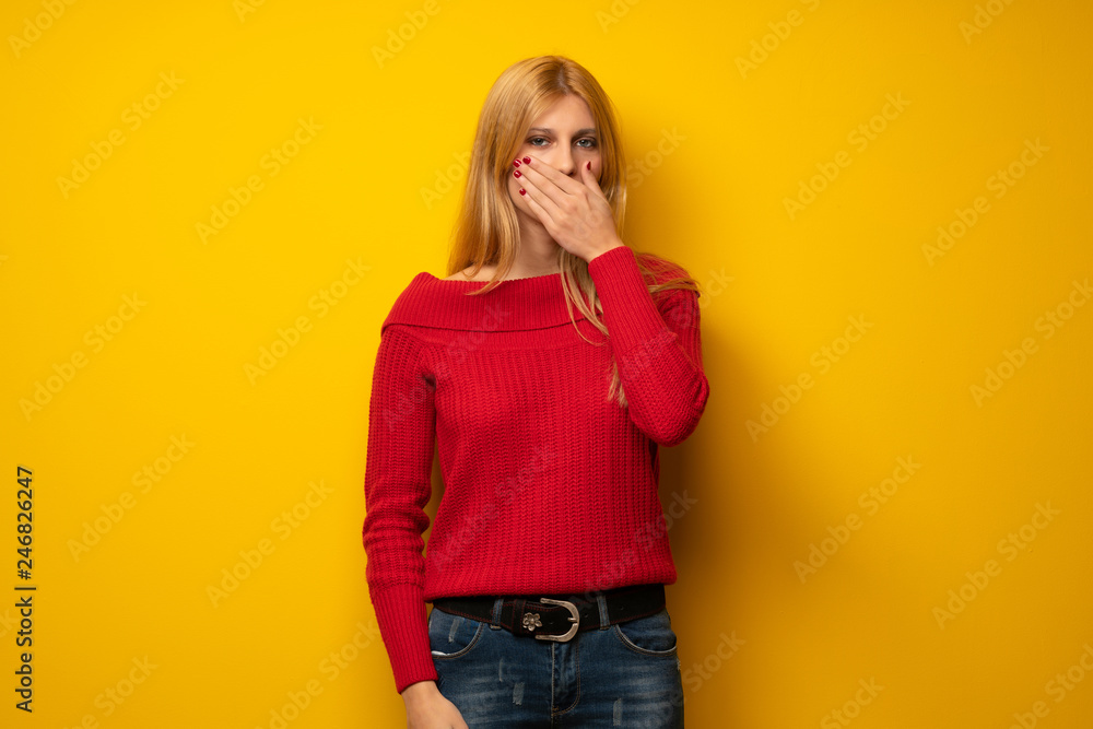 Blonde woman over yellow wall covering mouth with hands for saying something inappropriate