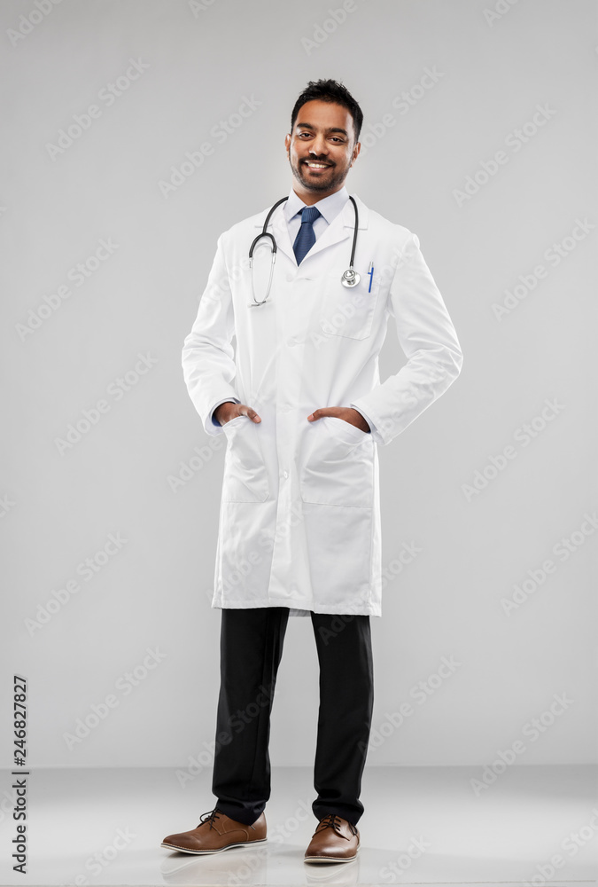 medicine, profession and healthcare concept - smiling indian male doctor in white coat with stethoscope over grey background medicine, profession and healthcare concept - smiling indian male doctor in white coat with stethoscope over grey background