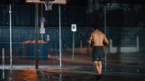 Athletic Young Male Basketball Player Dribbles and Throws the Ball in Crouched Position in a Residential Neighborhood Fenced Streetball Court.
