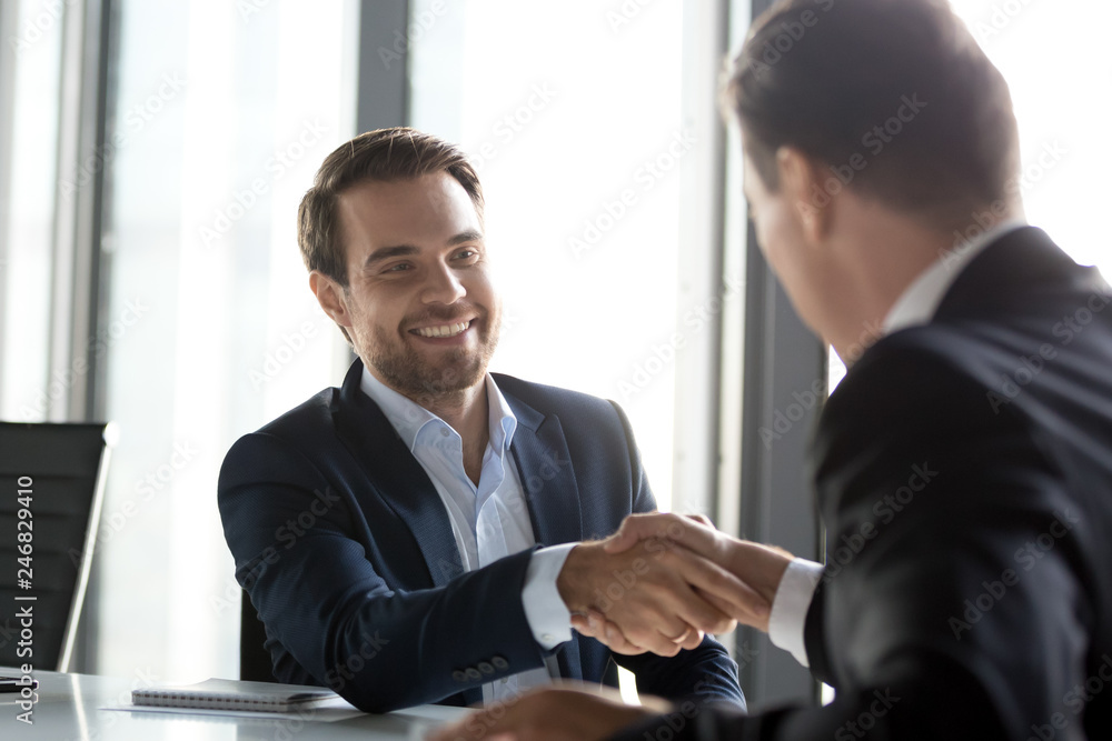 Happy businessmen in suits shaking hands after successful negotiations at meeting, male partners making business deal or good impression, thanking promising loyalty, respect gratitude handshake Happy businessmen in suits shaking hands after successful negotiations at meeting, male partners making business deal or good impression, thanking promising loyalty, respect gratitude handshake