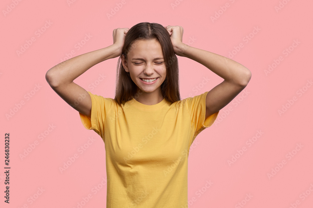 Studio shot of lucky schoolchild smiling broadly closing eyes and holding head with both hands, can believe that she got highest mark. Happiness, success and victory concept Studio shot of lucky schoolchild smiling broadly closing eyes and holding head with both hands, can believe that she got highest mark. Happiness, success and victory concept