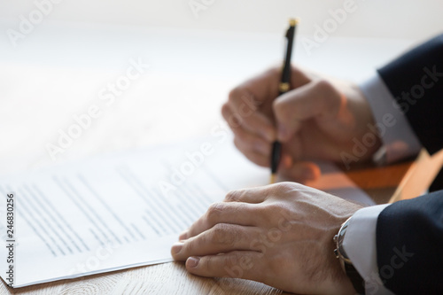 Close up view of male hand signing commercial financial contract concept, businessman put written signature on legal paper filling document form buy insurance, bank services, authorized registration