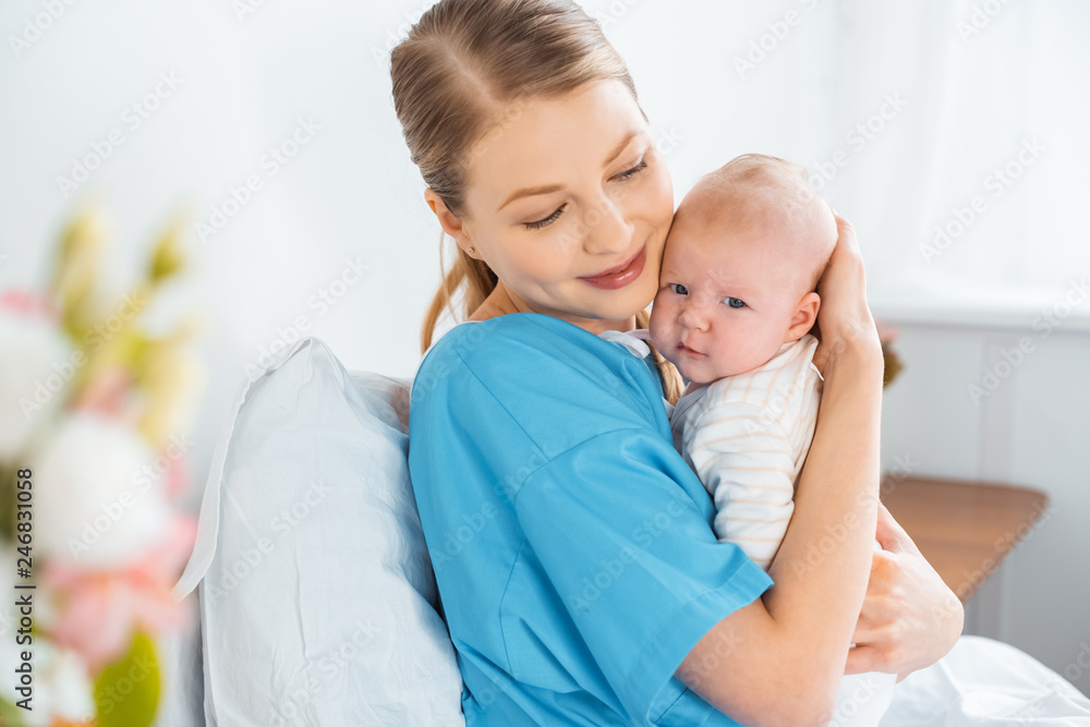 happy young mother sitting on hospital bed and hugging adorable baby happy young mother sitting on hospital bed and hugging adorable baby