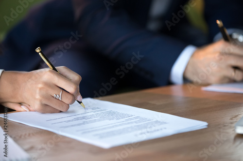 Close up view of woman and man signing document concluding contract concept making prenuptial agreement visiting lawyer office, female and male partners or spouses writing signature on decree paper photo