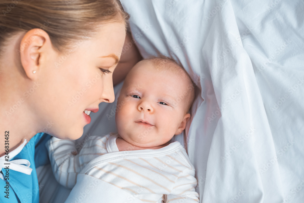 happy young mother looking at adorable newborn baby lying on bed happy young mother looking at adorable newborn baby lying on bed