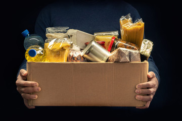 A man holding a donation box of different products on dark background