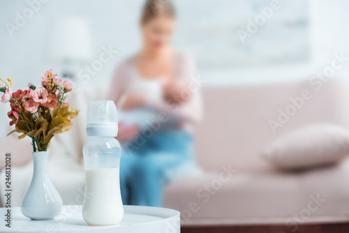 Foto close-up view of baby bottle with milk, flowers in vase and mother breastfeeding