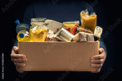 Fotótapéta A man holding a donation box of different products on dark background