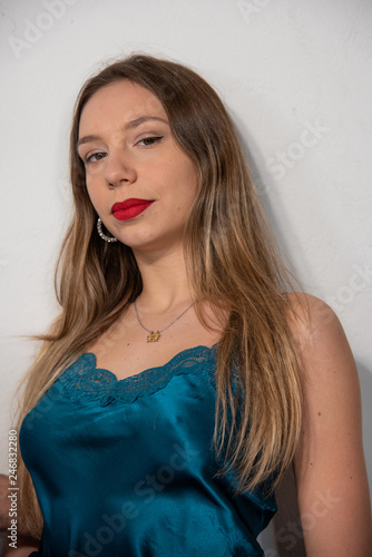 Half-length portrait of blonde girl in blue satin tank top with lace. Perfect makeup with red lips. White background. Copy space.