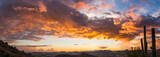 A panorama of a dramatic sunset over the desert with saguaro cactus and colorful clouds in the sky.