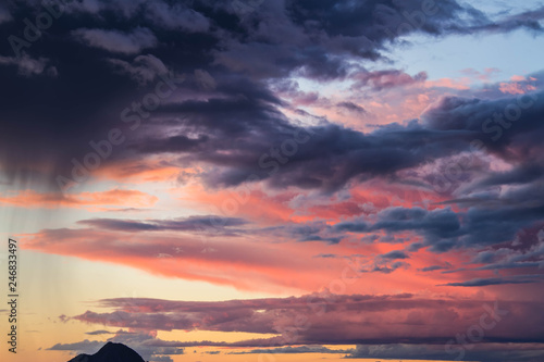 Clouds reflecting the light of a colorful sunset with a distant mountain at the bottom of the image.