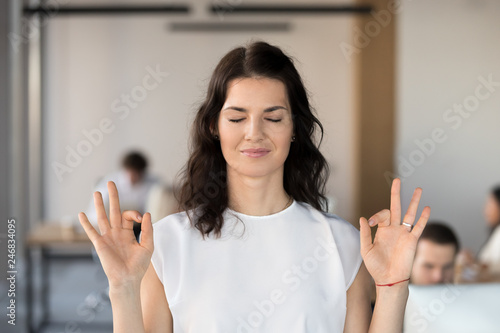 Young business woman employee meditating in office with eyes closed for no stress free relief, hoping for success, doing yoga exercise for relaxation or concentration at work, autosuggestion concept photo
