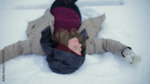 slow motion pretty girl in winterjacket with hood lays down in snow bunch and moves hands on cold winter day photo