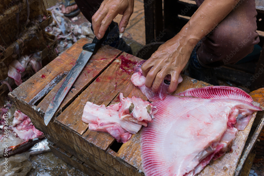 Male hands chopping fresh fish on a wooden box.