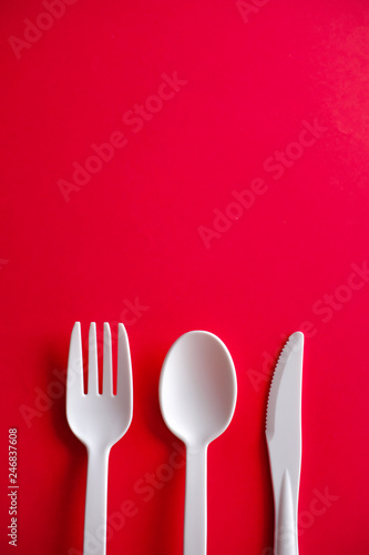 Minimalistic white reusable plastic spoon fork knife cutlery isolated on red background laying on the table with copy space. Top view flat lay perspective. Plastic concern.