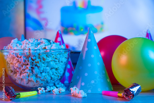 Popcorn with festive accessories on the background of TV. Watching TV on the occasion of a family celebration or in a circle of friends. Color and sevremenny light