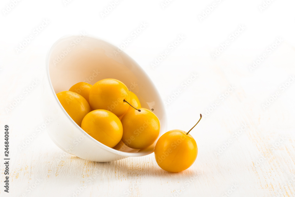 Handful of yellow cherry plums in ceramic bowl on white wooden surface Handful of yellow cherry plums in ceramic bowl on white wooden surface