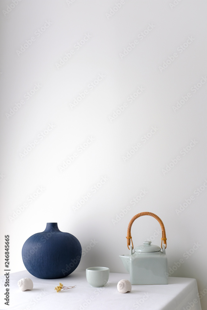 Japanese white ceramic teapot with wooden handle and tea cup and a blue oriental ceramic vase on white table top on white background in natural light with copy space. Minimal Asian interior styling.