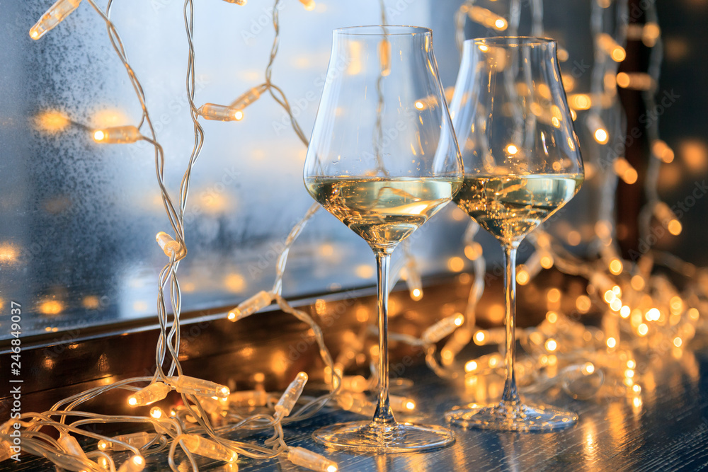 Closeup of two glasses of white wine in transparent crystal glasses on background of window and garlands. Concept romantic dinner in Michelin premium restaurant, party, February 14, March 8