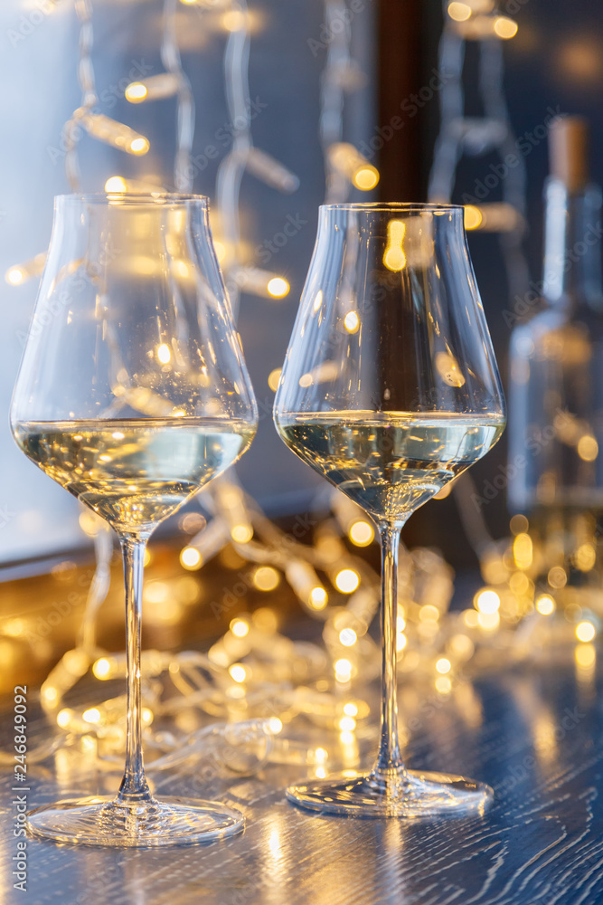 Closeup of two glasses of white wine in transparent crystal glasses on background of window and garlands. Concept romantic dinner in Michelin premium restaurant, party, February 14, March 8
