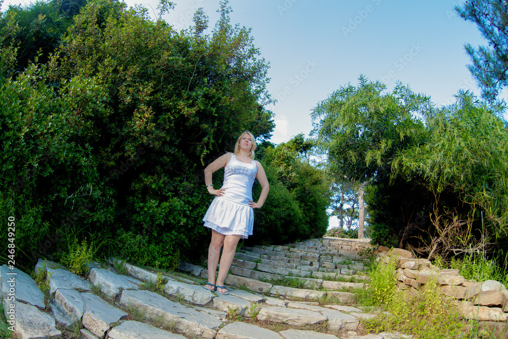 Young sexy blonde woman in white dress posing at the ladder outdoors in summer