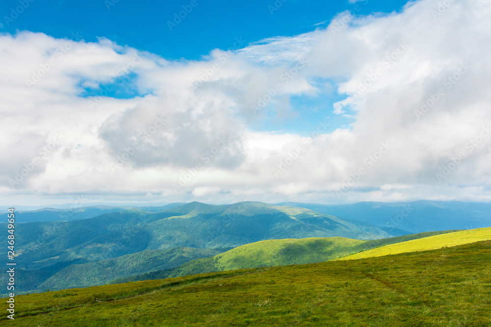 landscape in mountains. hills and meadows. sunny weather with beautiful cloudscape. grassy green slope and distant ridge.