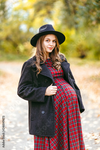 Beautiful autumn girl in the park. Lots of yellow leaves. Girl in a gray coat and red dress. Pregnant girl holding hands belly © sushytska