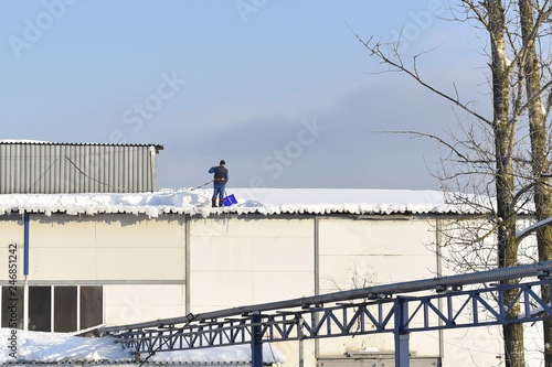 man removes snow from the roof of a building