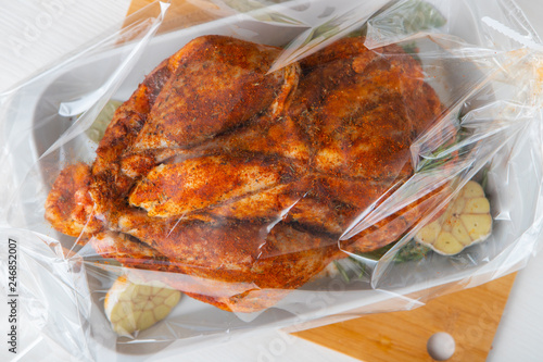 Raw guinea fowl smeared with spices with paprika lies on a white dish for baking with garlic and rosemary - all this lies in a transparent bag for baking