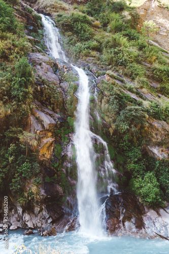 A waterfall spotted in Tal, Annapurna Circuit Trek, Nepal. Few hundred meters of free fall, waterfall surrounded by tall mountains slopes, covered with green bushes and trees. Smooth capture