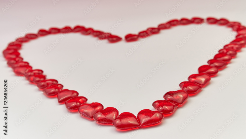 Heart-shaped laid out of small glass red hearts on white background. Valentine's Day. Symbol of love. Copy space. Heart-shaped laid out of small glass red hearts on white background. Valentine's Day. Symbol of love. Copy space.