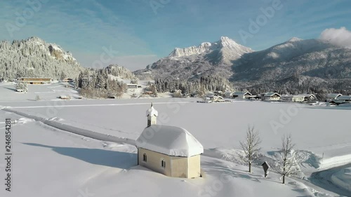 Aerial Drone shot showing a snowy landscape in in the sunshine of the Tyrol, Austria and a snow covered tiny chapel in Lechaschau. photo