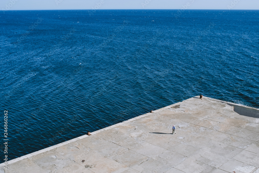 Man walking on a concrete dock on the coast of Adriatic Sea in Ulcinj, Montenegro.