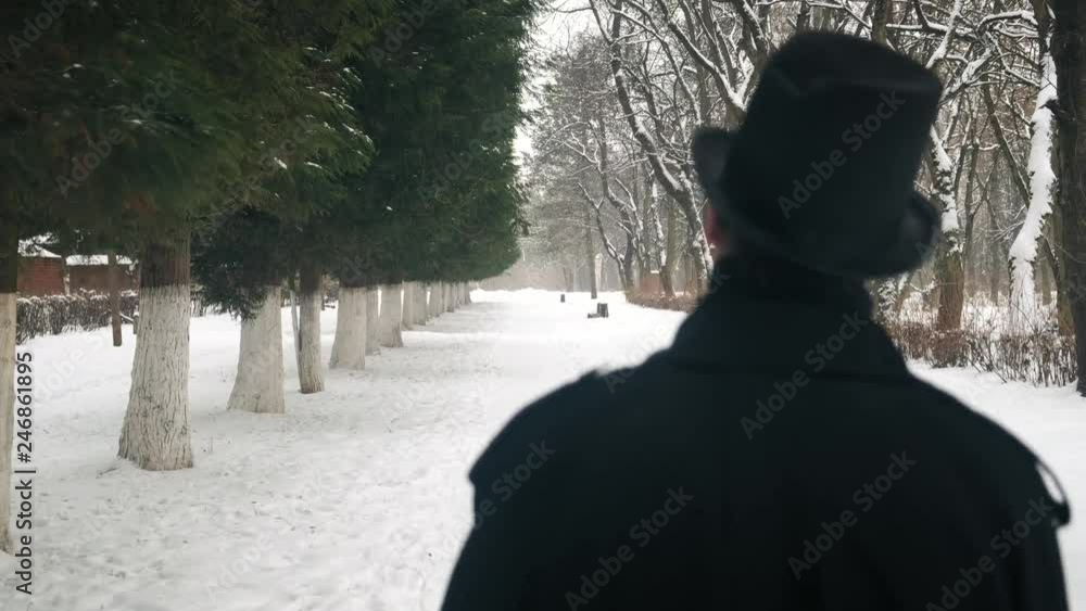 Middle view shot: A man in a black cloak and hat walks in the park alley. 60fps. 4k Middle view shot: A man in a black cloak and hat walks in the park alley. 60fps. 4k