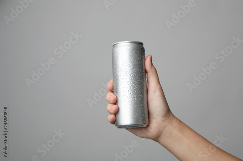 Woman holding aluminum can with beverage on grey background, closeup. Space for design photo